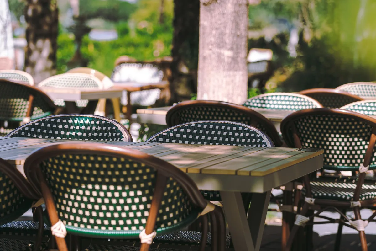 Tavoli di ristorante in spazio esterno ombreggiato con tende parasole e clienti che cenano