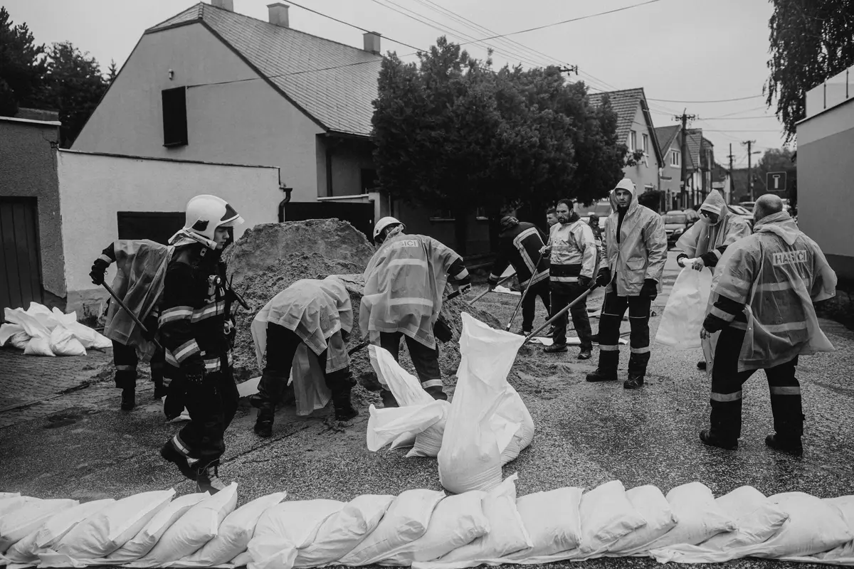 Squadre di emergenza al lavoro durante un'alluvione, con sacchi di sabbia e macchinari per il soccorso.