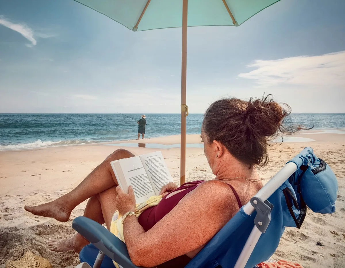 Libro aperto su una sedia a sdraio in spiaggia, con il mare sullo sfondo