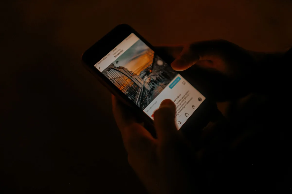 Mani che scorrono su uno schermo di smartphone mostrando un feed di social media con icone e notifiche.