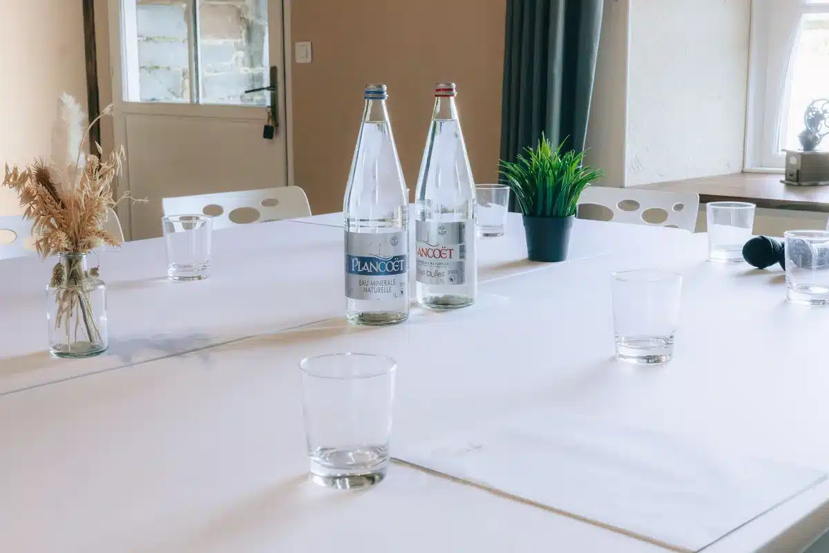 A wide empty meeting room with a single long table, stacked folders and a glass carafe of water on it