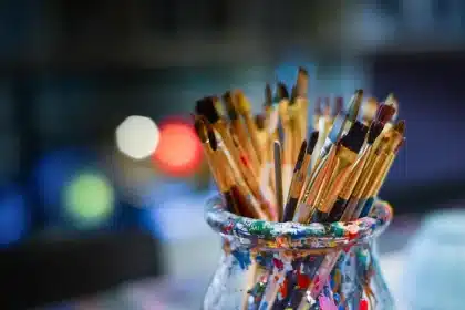 Mani anonime su un tavolo da lavoro con pennelli e schizzi, scena di studio artistico