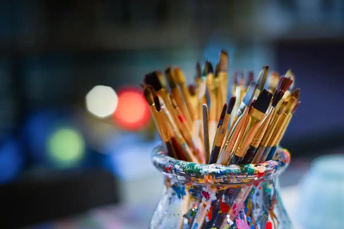 Mani anonime su un tavolo da lavoro con pennelli e schizzi, scena di studio artistico