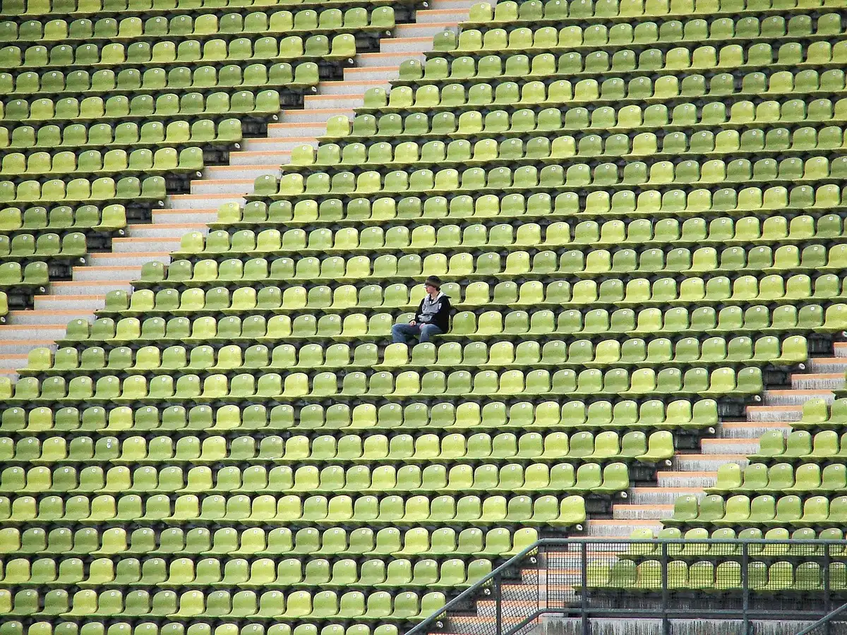 Empty stadium interior under floodlights, empty seats and a lone goal net visible