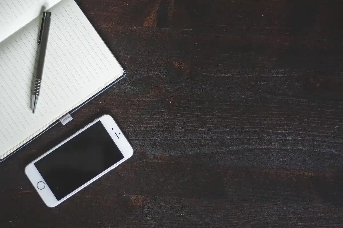 Mano anonima con libro e smartphone su tavolino in soggiorno, notifiche sfocate sullo schermo