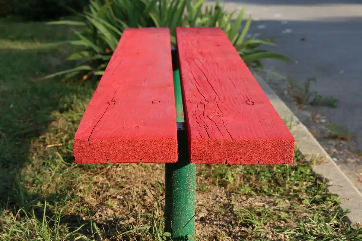 A lone red-painted bench on an empty urban square at dusk, no people visible, wet paving stones reflecting light