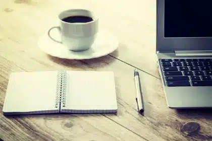 Scrivania con laptop e smartphone che mostrano titoli di notizie, tazza di caffè in vista
