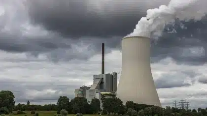 Ciminiera industriale con cumuli anonimi di rifiuti vicino, area industriale soleggiata