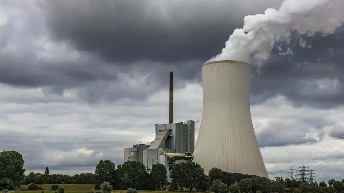 Ciminiera industriale con cumuli anonimi di rifiuti vicino, area industriale soleggiata