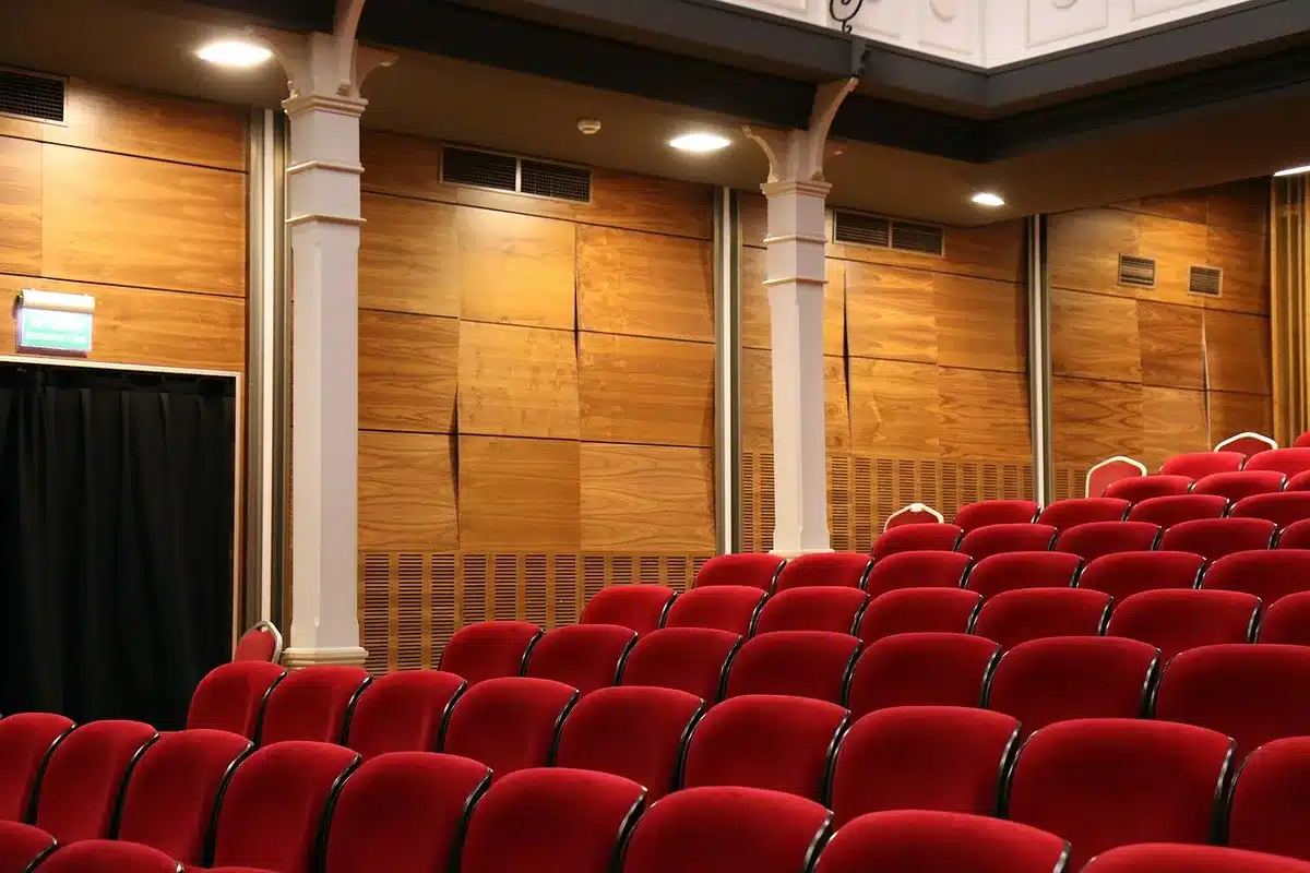 Interno di un teatro ristrutturato con palcoscenico e file di poltrone rosse