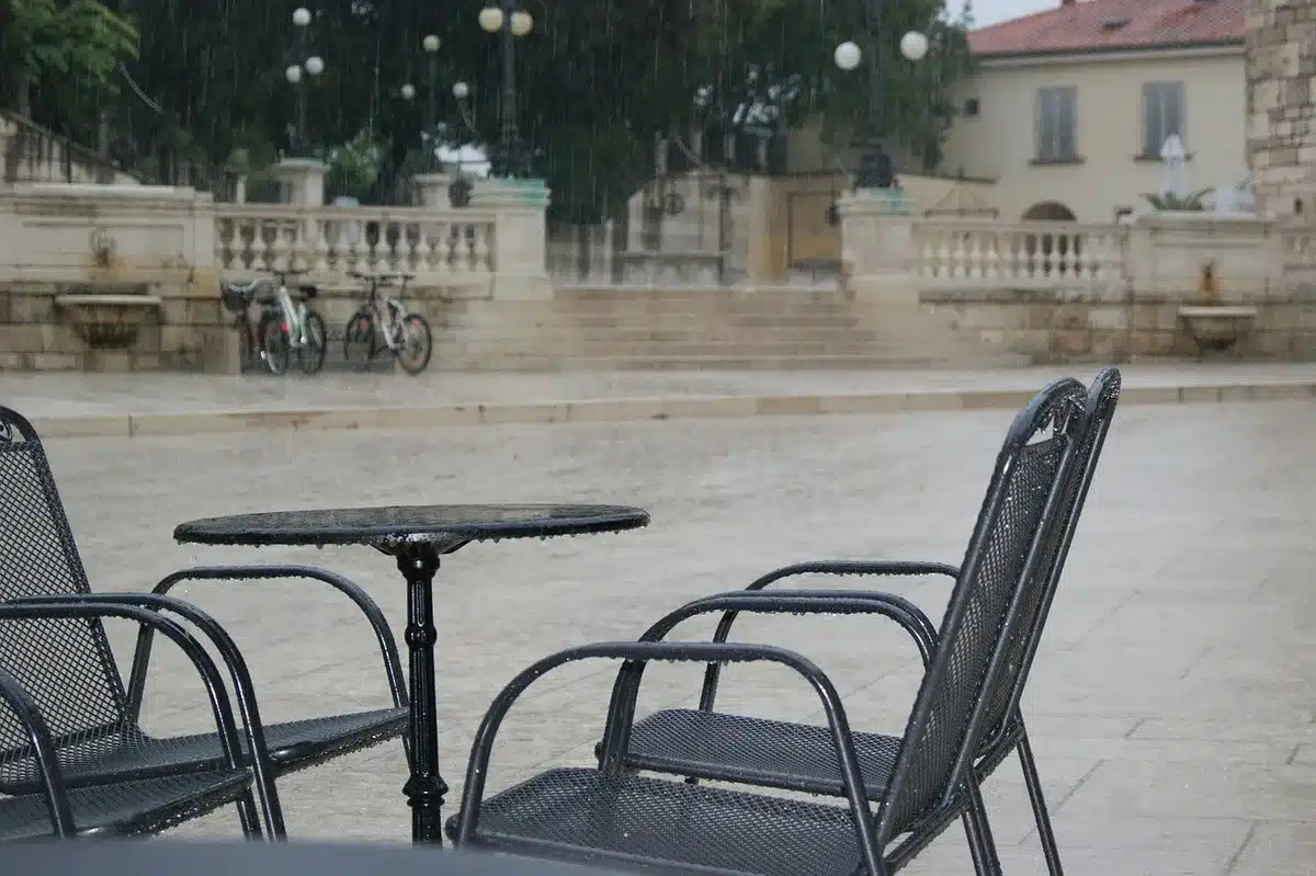 Empty urban square at dusk with a single overturned scooter and scattered paper cups, CCTV camera silhouette on a lamppost visible in the frame
