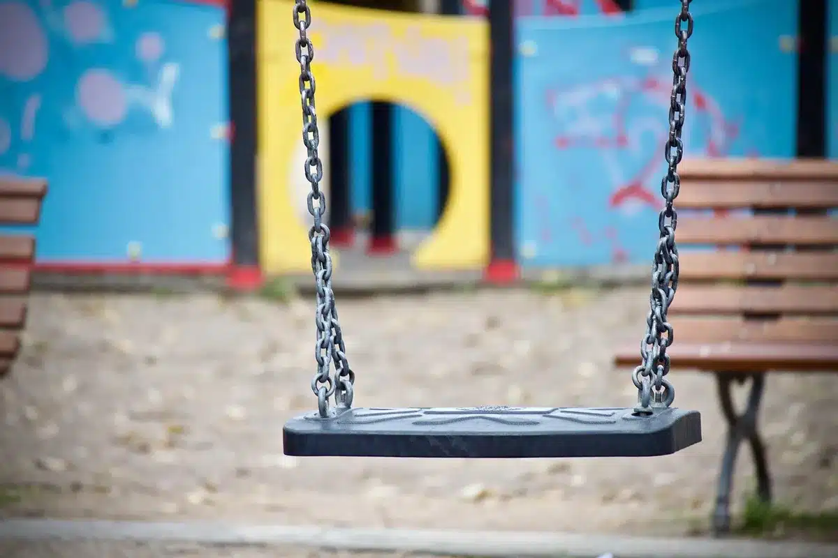 Parco giochi vuoto con uno zainetto su una panchina e due figure sullo sfondo
