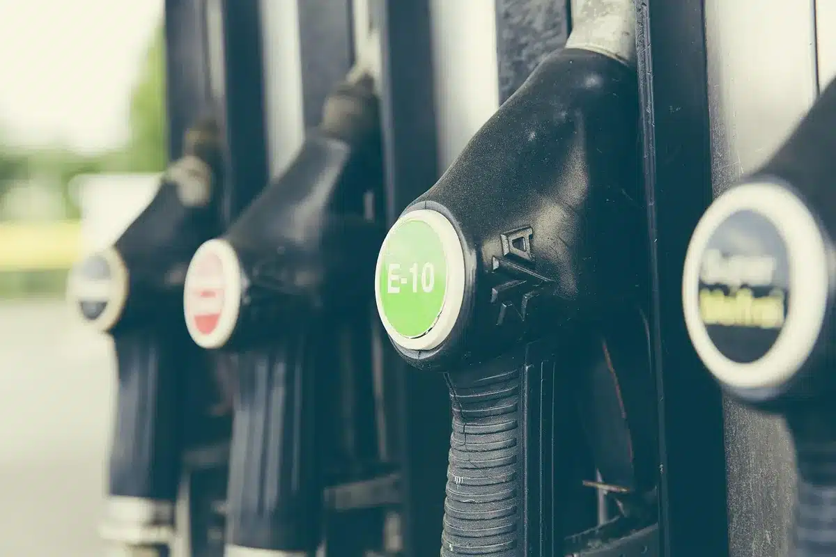 Empty fuel pumps at a deserted service station, no logos, a single fuel hose lying on the ground, wet asphalt reflecting streetlights