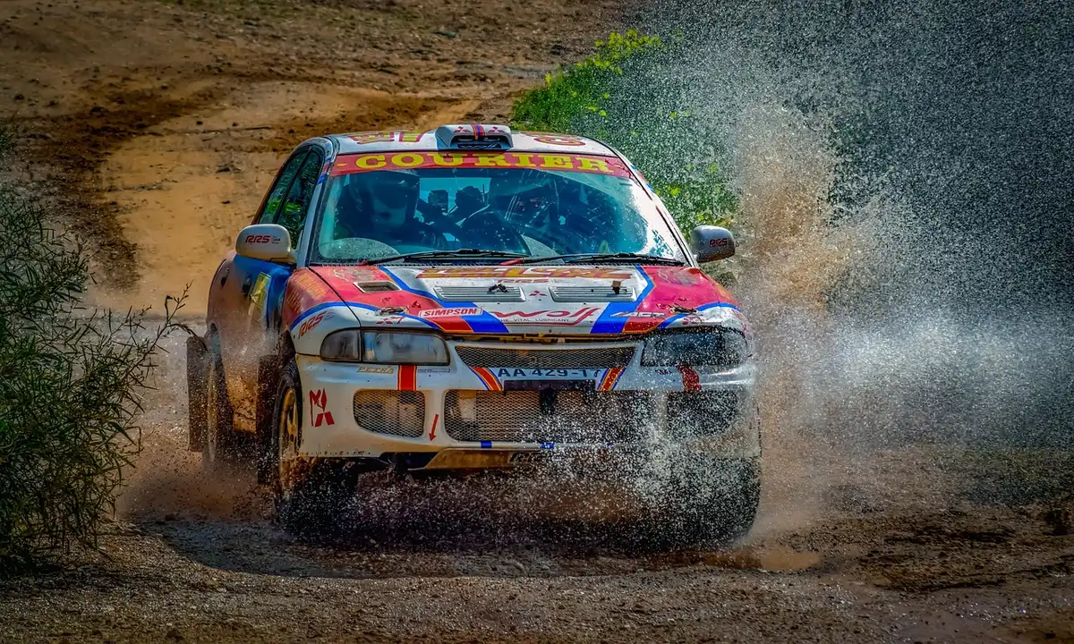 Anonymous group of mechanics around an unbranded rally car in a dim service park, spare wheels and toolboxes visible