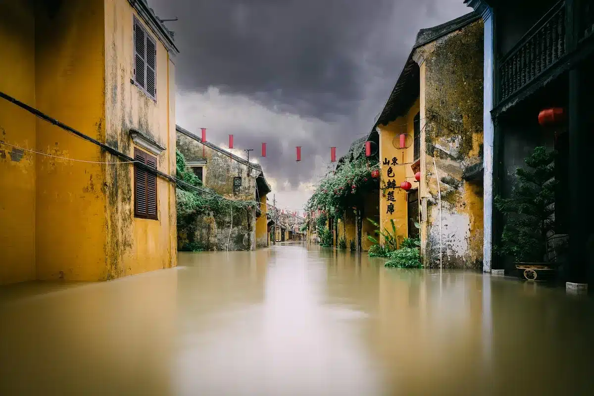 Empty urban street with rainwater flowing along gutters, a single anonymous umbrella left on a bench, low dark clouds over distant buildings