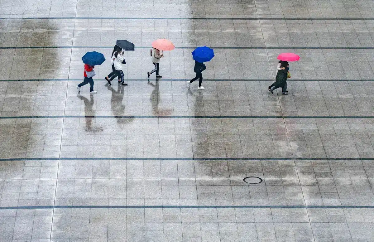 Empty piazza with wet pavement, a row of closed shopfronts and puddles reflecting streetlights, heavy cloud bank on the horizon
